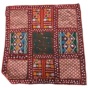 May include: A red, brown, and blue patchwork cushion cover with intricate embroidery and mirror embellishments. The cushion cover is made of a variety of fabrics and features a geometric pattern.