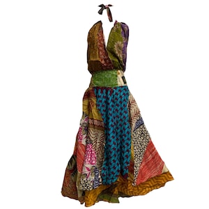 Può includere: Un abito halter in patchwork colorato con una gonna multicolore e un top verde, marrone e rosso. L'abito è realizzato con una varietà di tessuti e ha uno stile bohémien.