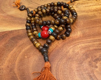 May include: A brown wooden mala bead necklace with red and turquoise beads. The necklace has a tassel at the end.
