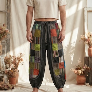 May include: Loose-fitting pants featuring a dark charcoal gray base with a patchwork design on the front panels. The patches include various colors like orange, lime green, and blue, along with woven patterns. The pants have an elastic waistband.