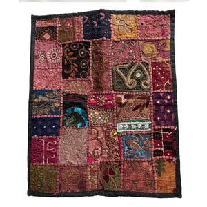 May include: A patchwork textile with a black border. The textile is composed of numerous squares in shades of pink, brown, and gold. Each square features unique embroidery, sequins, and beadwork, creating a textured and ornate design. The overall aesthetic is bohemian and decorative.