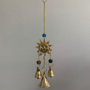 Op de afbeelding: Een gouden zon windgong met drie bellen en gekleurde kralen.
