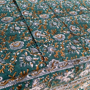 Peut inclure: Textile vert à motifs floraux blancs, gris et dorés. Le motif présente des fleurs et des vignes stylisées, créant un motif détaillé et orné. Les bords ont une bordure décorative.