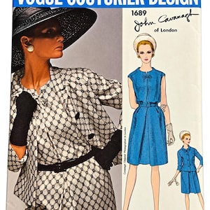 May include: Vogue Couturier Design 1689 John Cavanagh of London sewing pattern envelope. The front features a photograph of a person in a black and white patterned jacket and hat, alongside illustrations of a blue dress and a blue suit ensemble.