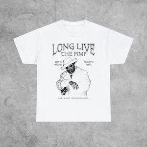 May include: White t-shirt with a black and white graphic print of a man wearing a hat and suit. The text "Long Live The Pimp" is at the top of the graphic. The text "Rest in Paradise" and "Tribute to Pimp C" are on the left and right sides of the graphic, respectively. The text "Rap-A-Lot Records, Inc." is at the bottom of the graphic.