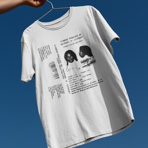 May include: White t-shirt with a black and white image of a mugshot. The mugshot is for Tommy Wright III, and the text "Runnin-N-Gunnin" is printed above the image. The text "Street Smart Records" is printed below the image.