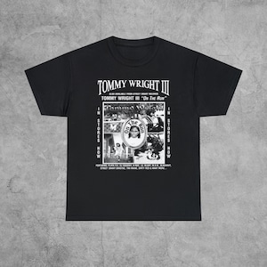 May include: Black and white graphic t-shirt featuring a collage of images and text. The text reads "Tommy Wright III" and "On The Run".