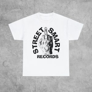 May include: White t-shirt with a black and white graphic of a hand giving the middle finger with the text "STREET SMART RECORDS" around it.