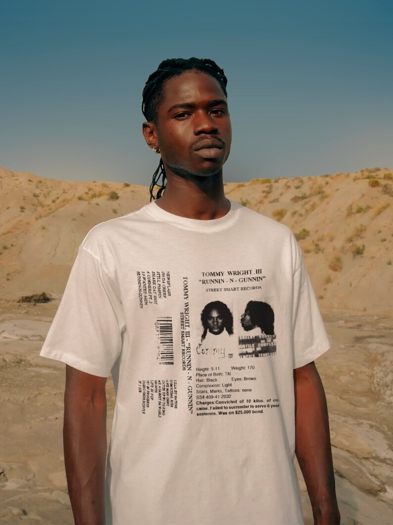 May include: White t-shirt with a black and white image of a mugshot on the back. The mugshot is labeled "Tommy Wright III - "Runnin-N-Gunnin" Street Smart Records". The text below the mugshot includes details like height, weight, place of birth, hair color, complexion, eyes, scars, marks, tattoos, social security number, charges, and sentence.
