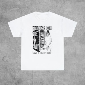 May include: White t-shirt with a black and white graphic print of a woman standing in front of a refrigerator with the words "Princess Loko", "Street Smart", and "Game Recognize Game" printed on it.