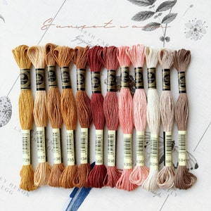 May include: A collection of 12 embroidery floss spools in shades of brown, red, pink, and beige. The spools are labelled with numbers, including 1729, 437, 436, 435, 434, 355, 356, 6352, 6353, ECRU, 684, and 6840.
