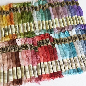 May include: A collection of embroidery floss spools in various colours, including white, yellow, orange, green, blue, purple, pink, red, brown, and grey. The spools are arranged in rows and columns, with the colour gradient changing from left to right.