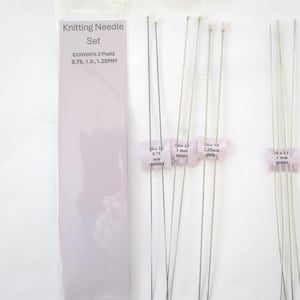 May include: A knitting needle set with three pairs of needles in sizes 0.75, 1.0, and 1.25mm. The needles are silver-colored and come with a lavender-colored package that has the text "Knitting Needle Set".