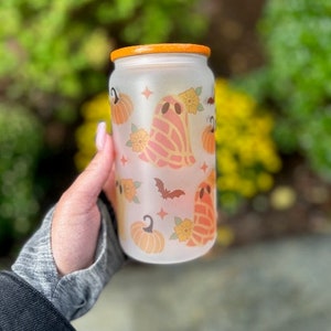 May include: A frosted glass water bottle with an orange lid and a Halloween-themed design. The design features ghosts, pumpkins, bats, and flowers in orange, yellow, and white.