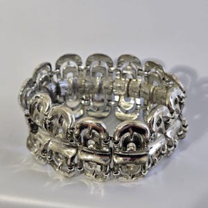Puede incluir: Una pulsera de metal plateado con un patrón repetitivo de eslabones arqueados interconectados. El diseño consta de dos filas de estos segmentos curvos y pulidos unidos para formar una banda ancha y flexible con acabado texturizado.