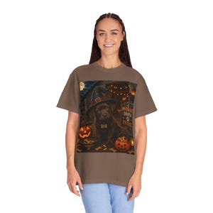 Pode incluir: Uma t-shirt castanha com um gráfico de um cachorro preto a usar um chapéu de bruxa, rodeado por abóboras e um sinal que diz Midnight Snack Patrol. O design inclui uma taça com a etiqueta Treats e doces espalhados pelo chão.