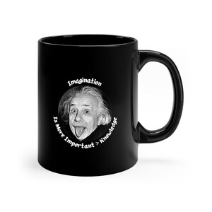 Pode incluir: Caneca de café preta com um design circular branco que apresenta uma foto de Albert Einstein com a língua de fora e o texto "Imagination Is More Important > Knowledge".