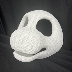 May include: A white, textured, 3D-printed mask with large eye and mouth openings. The mask has a rounded shape with a prominent nose and a textured surface. The mask is likely for cosplay or costume use.