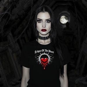 May include: Black t-shirt with the text "Eclipse Of The Heart" above a graphic of a bleeding heart. The design is in red and white. The model is wearing a black lace choker.