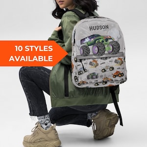 Może przedstawiać: Szary plecak z zielono-fioletowym wzorem monster trucka, z imieniem "Hudson" wydrukowanym na górze. Plecak ma wzór mniejszych monster trucków. Obraz zawiera również tekst "10 STYLES AVAILABLE".