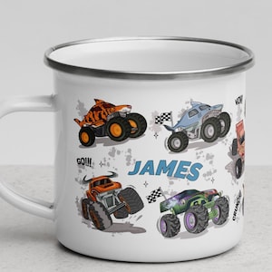 May include: White enamel camping mug with a silver rim. The mug features a colorful cartoon design of monster trucks with the name "JAMES" printed on the side. The text "GO!!!" and "WOW!" are also printed on the mug.