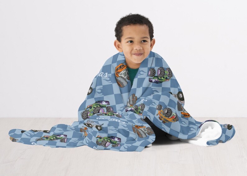May include: A blue and white checkered fleece blanket with a monster truck design. The blanket features a variety of monster trucks in different colors and designs. The blanket is wrapped around a child.