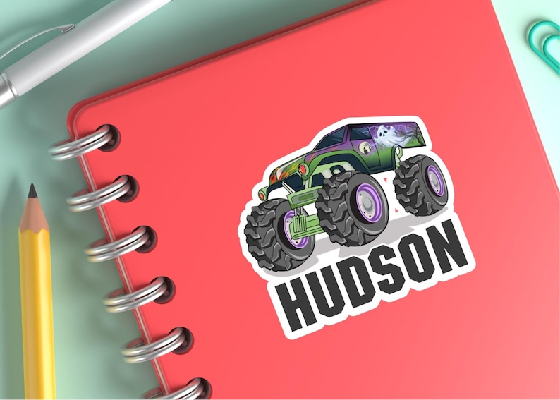 May include: A sticker featuring a cartoon monster truck with large tires, green and purple accents, and a ghost graphic. The name "HUDSON" is printed in bold, white letters below the truck.