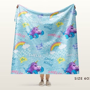 May include: A blue fleece blanket with a unicorn and rainbow pattern. The blanket features the name "Amelia" and the phrase "One of a Kind" repeated throughout. The blanket is 60 inches by 80 inches.