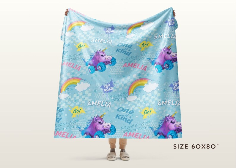 May include: A blue fleece blanket with a unicorn and rainbow pattern. The blanket features the name "Amelia" and the phrase "One of a Kind" repeated throughout. The blanket is 60 inches by 80 inches.