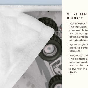 Op de afbeelding: Een wit, fluweelzacht minky deken met een cartoon monstertruck ontwerp. De tekst "VELVETEEN MINKY BLANKET" is zichtbaar aan de rechterkant van de afbeelding. Het deken wordt beschreven als zacht, hypoallergeen en gemakkelijk te onderhouden.