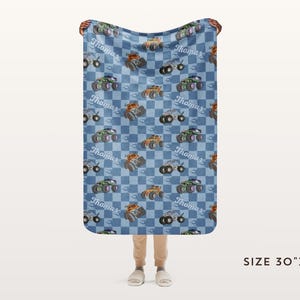 May include: A blue and white checkered fleece blanket with a repeating pattern of monster trucks and the name "Thomas". The blanket is 30 inches by 40 inches.