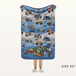 May include: A blue blanket with a pattern of colorful monster trucks, with phrases like "WOW!" and "CRUNCH!" scattered across the design. The blanket measures 30" x 40".