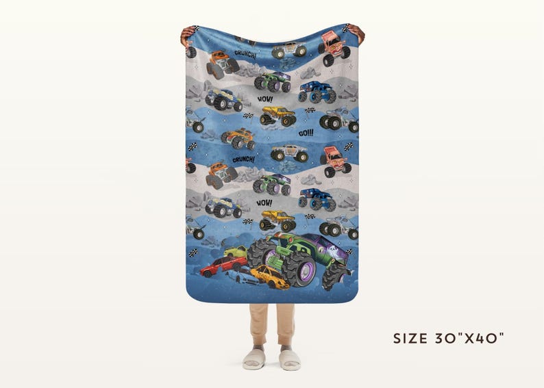 May include: A blue blanket with a pattern of colorful monster trucks, with phrases like "WOW!" and "CRUNCH!" scattered across the design. The blanket measures 30" x 40".