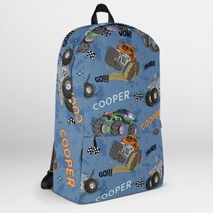 May include: Blue backpack with a monster truck pattern. The backpack features the name "COOPER" repeated throughout the design, along with phrases like "GO!" and "WOW!" The monster trucks are orange, green, and blue.