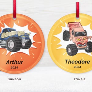 May include: Two round Christmas ornaments with red ribbon hangers. One is orange with a blue monster truck and the name "Arthur" and the year "2024". The other is yellow with a pink monster truck and the name "Theodore" and the year "2024".