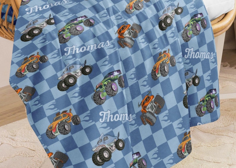May include: Blue and white checkered fleece blanket with a repeated pattern of monster trucks. The blanket features the name "Thomas" repeated throughout.
