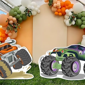 Op de afbeelding: Twee cartoon monstertrucks, een oranje en een groene, met grote wielen en een spookgrafiek op de groene truck. De trucks staan voor een achtergrond van oranje, beige en witte ballonnen.