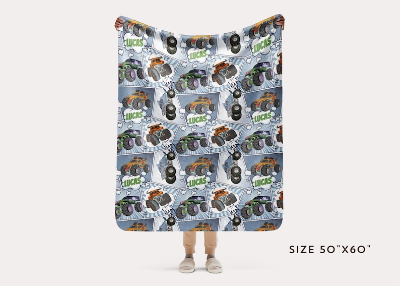 Puede incluir: Una manta de franela azul y blanca con un patr&oacute;n repetido de monster trucks. Los camiones son verdes, naranjas y negros con el nombre "Lucas" en un bocadillo. La manta mide 127 cm por 152 cm.