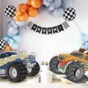Op de afbeelding: Twee cartoon monstertruck-uitknipsels, een blauwe met gele accenten en een oranje met bruine accenten. Beide trucks hebben grote banden en een tandenrij. De trucks staan voor een witte muur met een zwart-wit geblokte ballonboog en een zwart spandoek met de tekst "VROOM!"