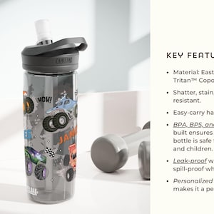 May include: A clear water bottle with a black lid and a gray handle. The bottle is decorated with colorful monster truck graphics and the name "JAMES". The bottle is made of Eastman Tritan Copolyester.