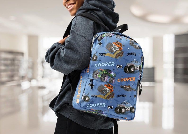 May include: A blue backpack with a monster truck pattern. The backpack has the name "COOPER" printed on it multiple times. The backpack has orange, black, and white accents.