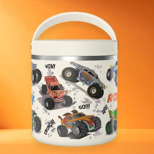 Könnte beinhalten: Ein cremefarbener isolierter Lebensmittelbehälter mit weißem Griff und einem Muster aus bunten Monstertrucks. Das Design zeigt Illustrationen verschiedener Trucks, Zielflaggen sowie die aufgedruckten Wörter "WOW!", "GO!!!" und "CRUNCH!" auf der Oberfläche.