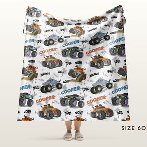 May include: A white fleece blanket featuring a repeating pattern of monster trucks in various colours, including orange, blue, and green. The trucks have the word "COOPER" printed on them, along with phrases like "WOW!" and "CRUNCH!" The blanket measures 60 inches by 80 inches.