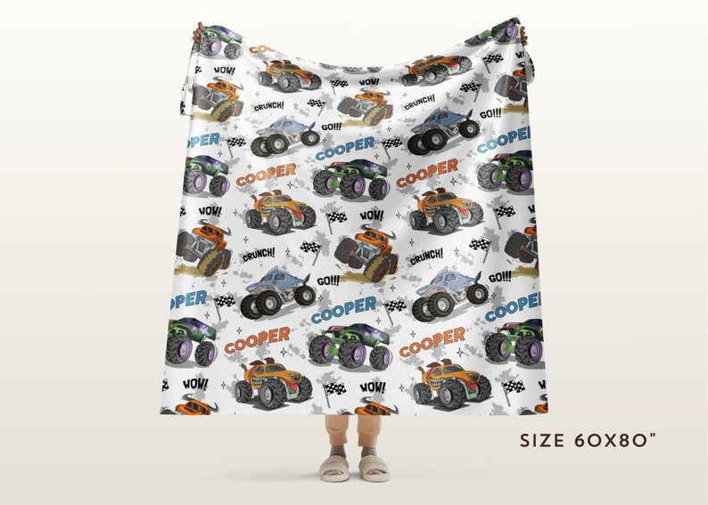 May include: A white fleece blanket featuring a repeating pattern of monster trucks in various colours, including orange, blue, and green. The trucks have the word "COOPER" printed on them, along with phrases like "WOW!" and "CRUNCH!" The blanket measures 60 inches by 80 inches.