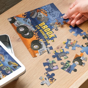 May include: A personalized jigsaw puzzle with a monster truck theme. The puzzle features a blue and orange design with the text "BROOK 5TH MONSTER JAM". A matching image is on a tablet next to the puzzle.