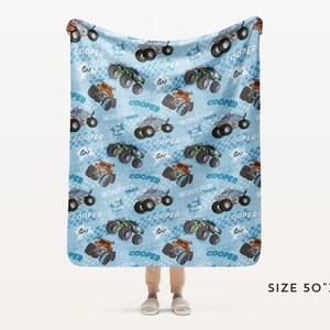 Pu&ograve; includere: Una coperta in pile blu e bianca con un motivo ripetitivo di monster truck. I camion sono blu, neri e arancioni con la scritta "COOPER" stampata su di essi. La coperta misura 127 cm per 152 cm.