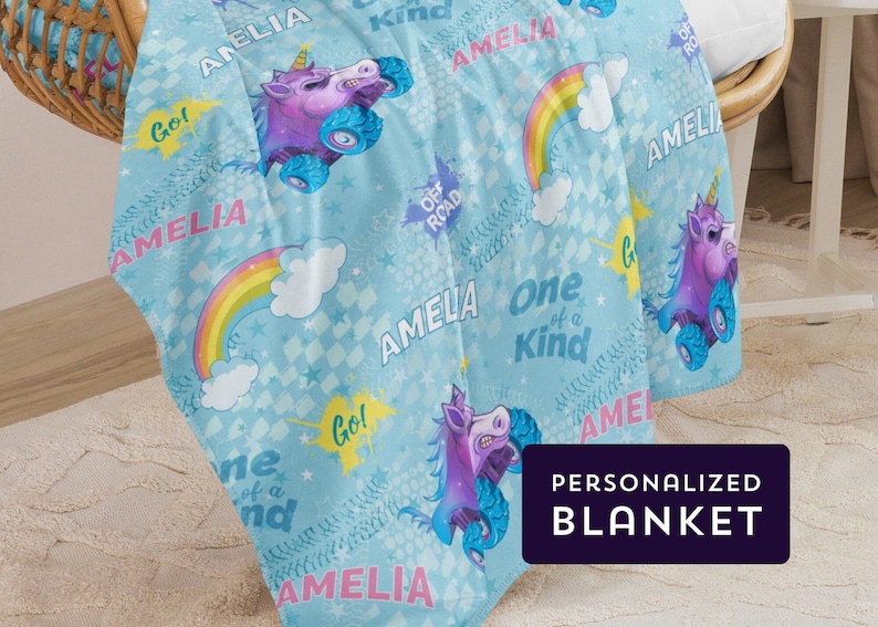 May include: A blue personalised blanket with a unicorn design. The blanket features rainbows, stars, and the text "Amelia" and "One of a Kind".