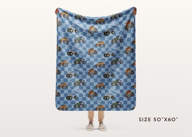 May include: A blue and white checkered fleece blanket with a repeated pattern of monster trucks. The trucks are orange, black, and gray with white wheels. The blanket is personalized with the name "Thomas" repeated throughout the pattern. The blanket is 50 inches by 60 inches.
