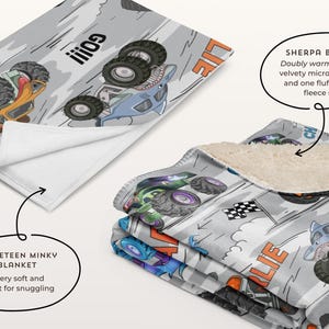 May include: A grey blanket with a monster truck design. The blanket has a soft, velvety microplush side and a fluffy sherpa fleece side. The design includes monster trucks, the word "GO!!!", and the word "LIE".