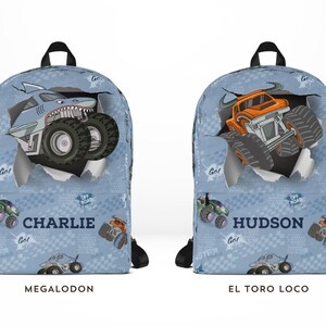 May include: Two blue backpacks with black straps. One features a shark-themed monster truck, the other an orange monster truck. Both have the names "Charlie" and "Hudson" printed on them, with the monster truck names "Megalodon" and "El Toro Loco".